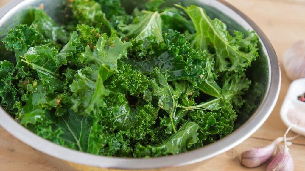 Eine Nahaufnahme einer silbernen Schüssel, gefüllt mit frischem, krausem Grünkohl auf einem Holztisch.