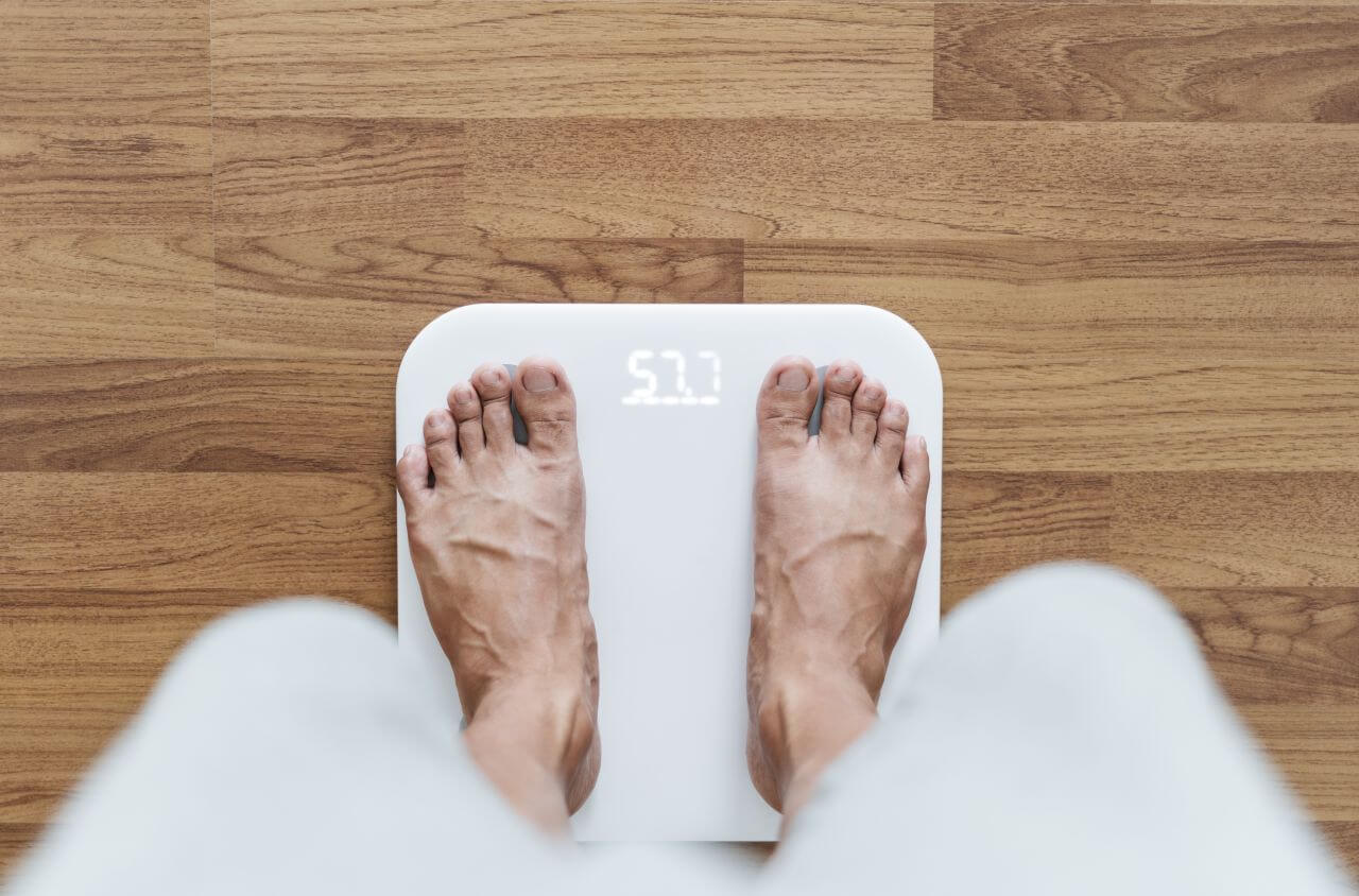 Füße, die auf einer weißen digitalen Personenwaage stehen.