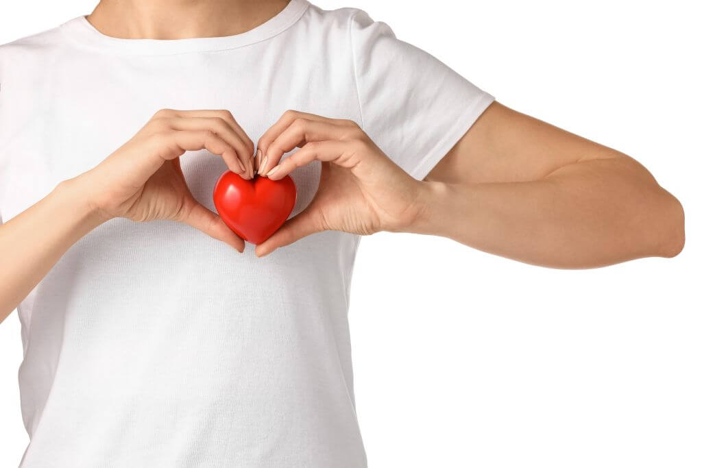 Eine Person hält ein kleines rotes Herz in ihren Händen vor einem weißen T-Shirt.