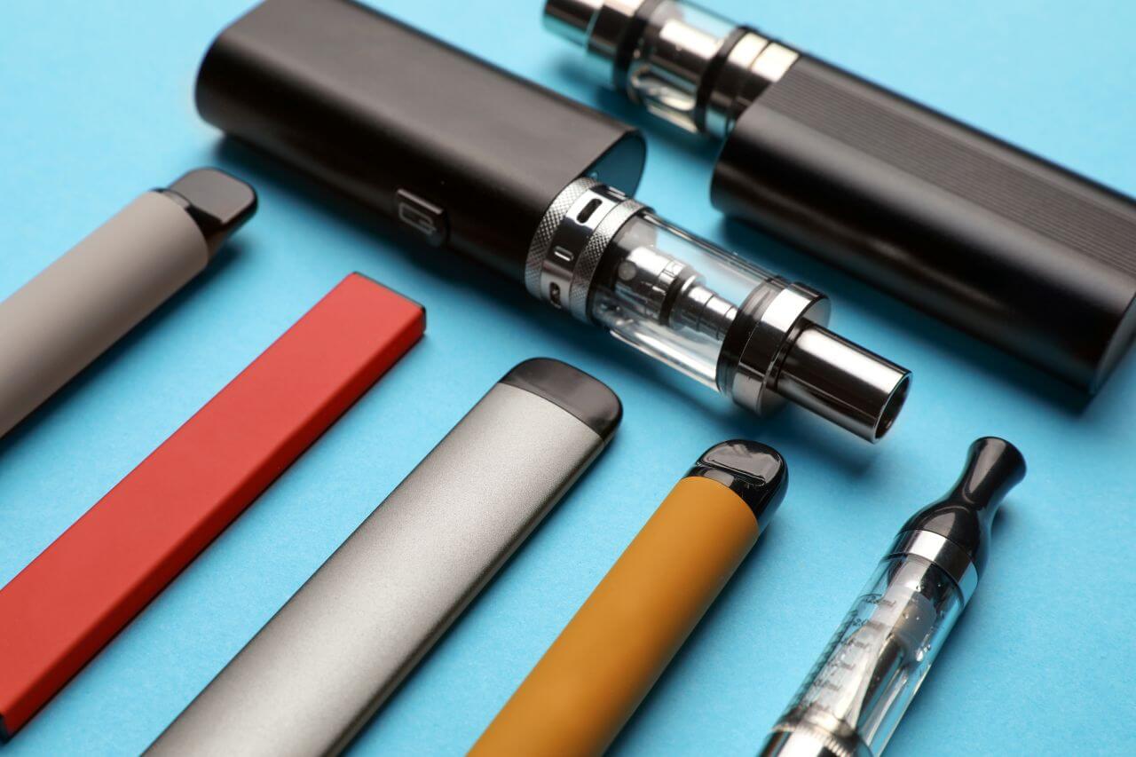 Unterschiedliche Arten von E-Zigaretten und Vapes auf hellblauem Hintergrund.