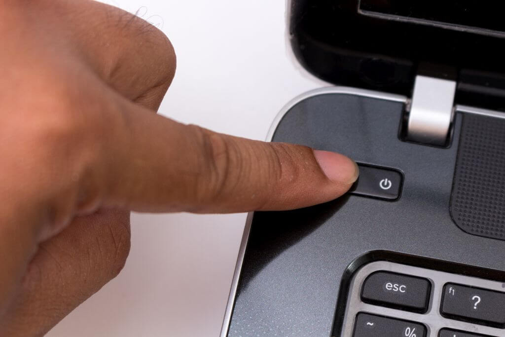 Ein Finger drückt auf den Einschaltknopf eines Laptops.