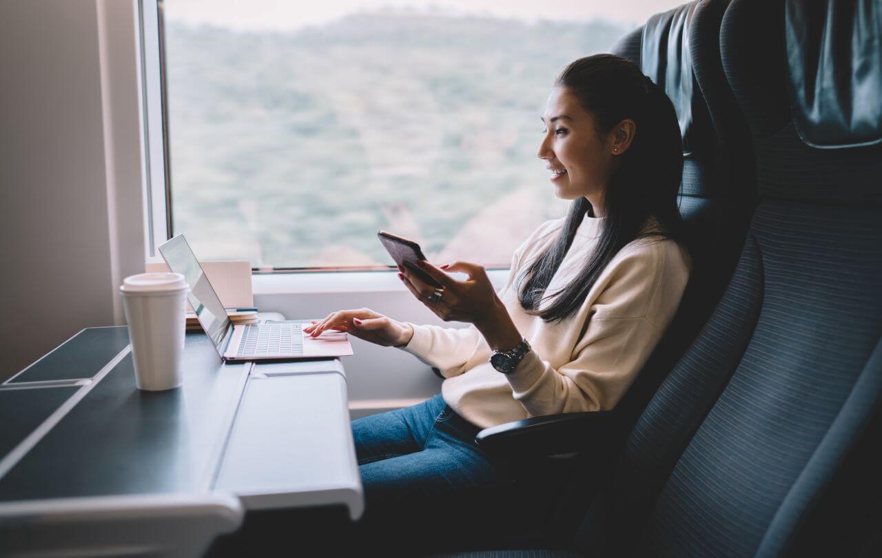 Frau sitzt in einer Bahn und arbeitet am Laptop.