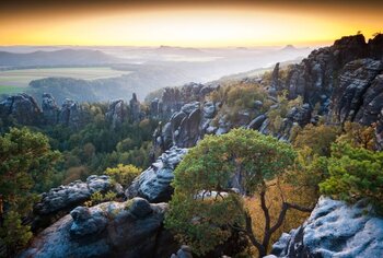 Eine weite Landschaft mit zerklüfteten Felsformationen und grünen Bäumen unter einem leuchtenden Horizont.