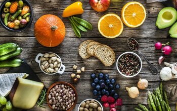 Eine vielfältige Auswahl an Obst, Gemüse, Käse, Brot und Nüssen auf Holzuntergrund.