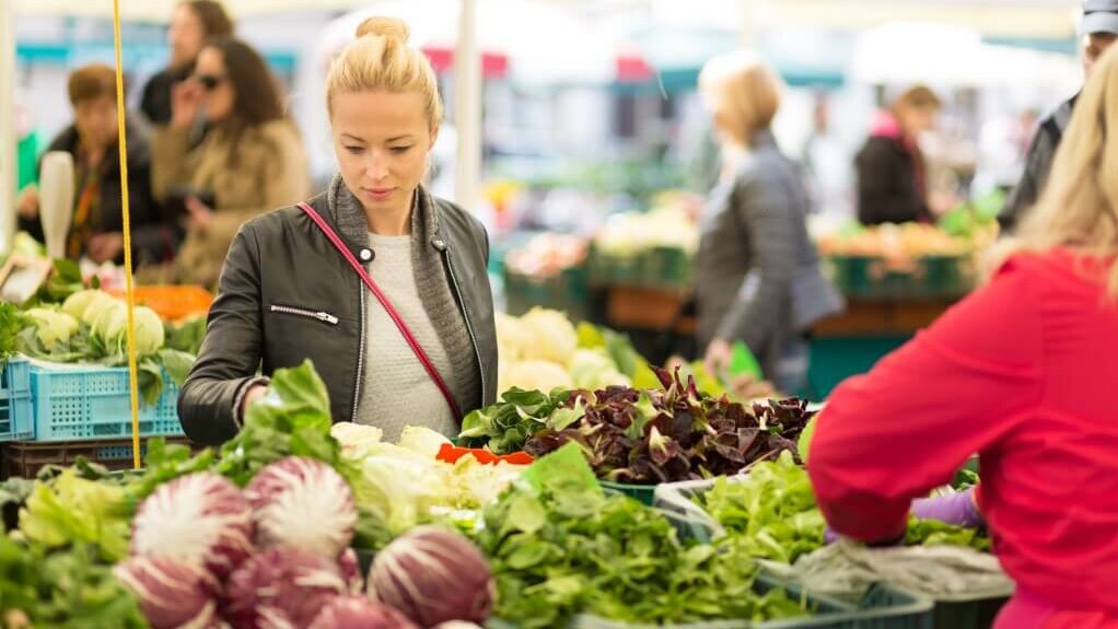 Eine Frau wählt auf einem Wochenmarkt frisches Gemüse aus.