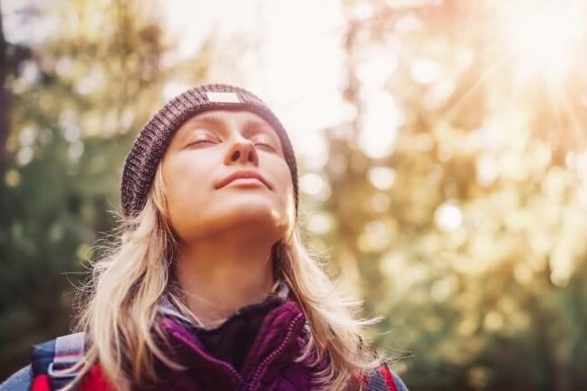 Eine Person genießt die Sonne im Wald, die Augen geschlossen, in einem Moment der Ruhe und des Friedens.