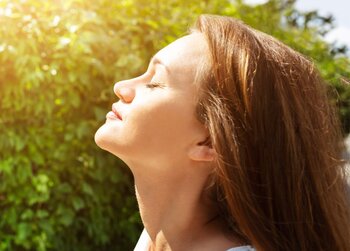 Profilansicht einer Person, die ihre Augen geschlossen hält und ihr Gesicht dem warmen Sonnenlicht zuwendet.