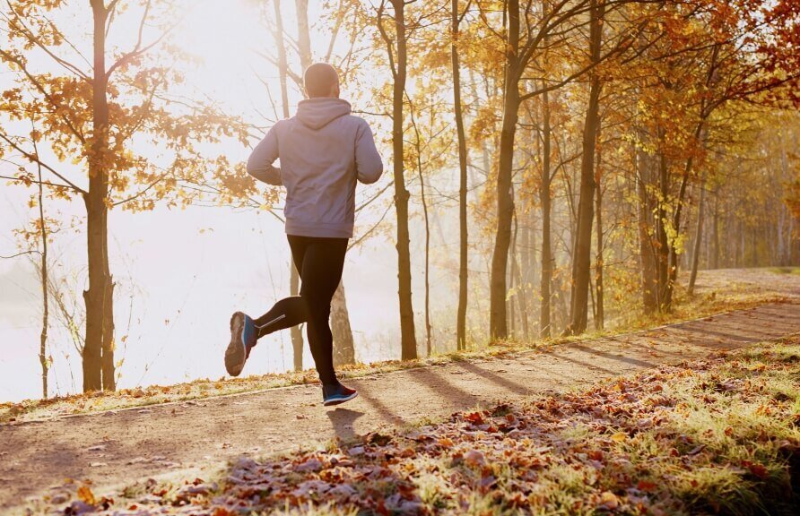 Eine Person läuft auf einem Pfad durch einen sonnigen Herbstwald.