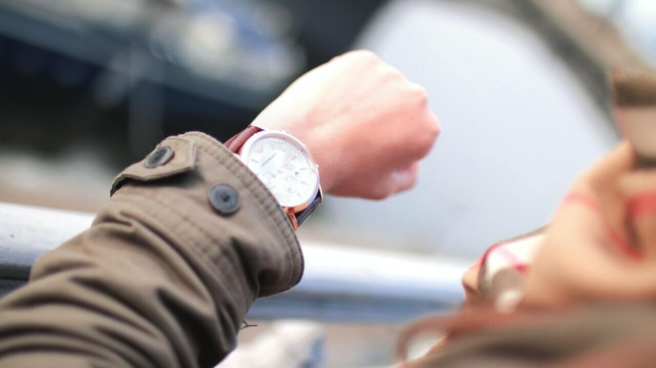 Nahaufnahme einer Hand, die auf eine Armbanduhr blickt.
