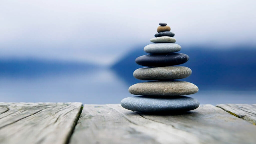 Ein Turm aus gestapelten Steinen auf einem Holzsteg vor einem nebligen See.