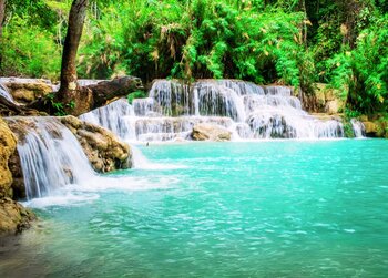 Stufenförmiger Wasserfall, der in ein leuchtend türkises Becken in einem üppig grünen, tropischen Wald mündet.