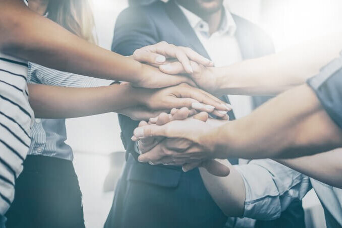 Mehrere Hände liegen übereinander, was Zusammenhalt, Teamarbeit und Einheit symbolisiert.