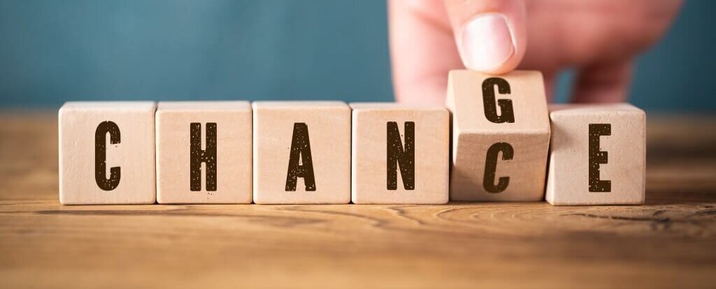 Eine Hand ändert Holzklötze, die "CHANCE" buchstabieren, zu "CHANGE", symbolisiert Transformation.